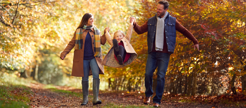 Parents holding up their child among fall leaves.