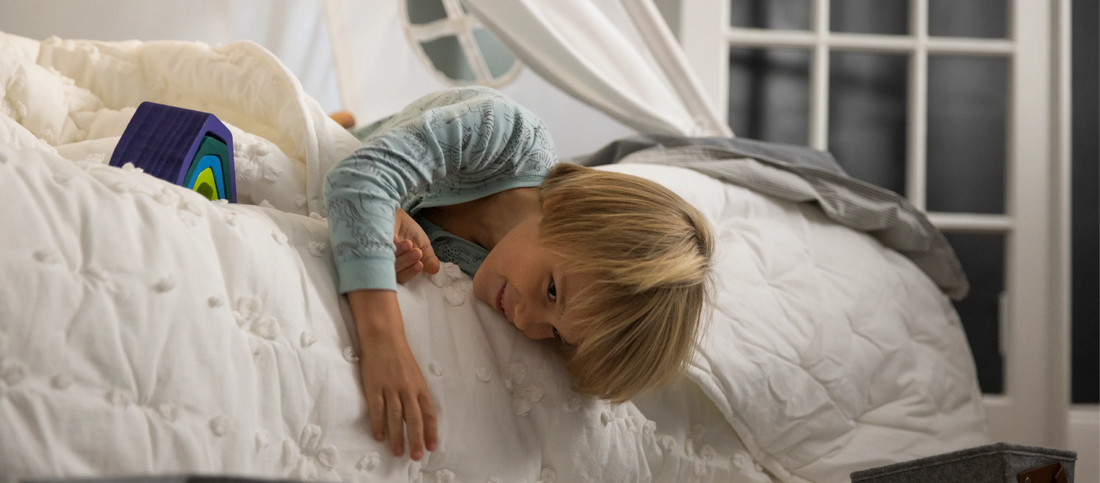 Child relaxing on a bed with a stackable toy.